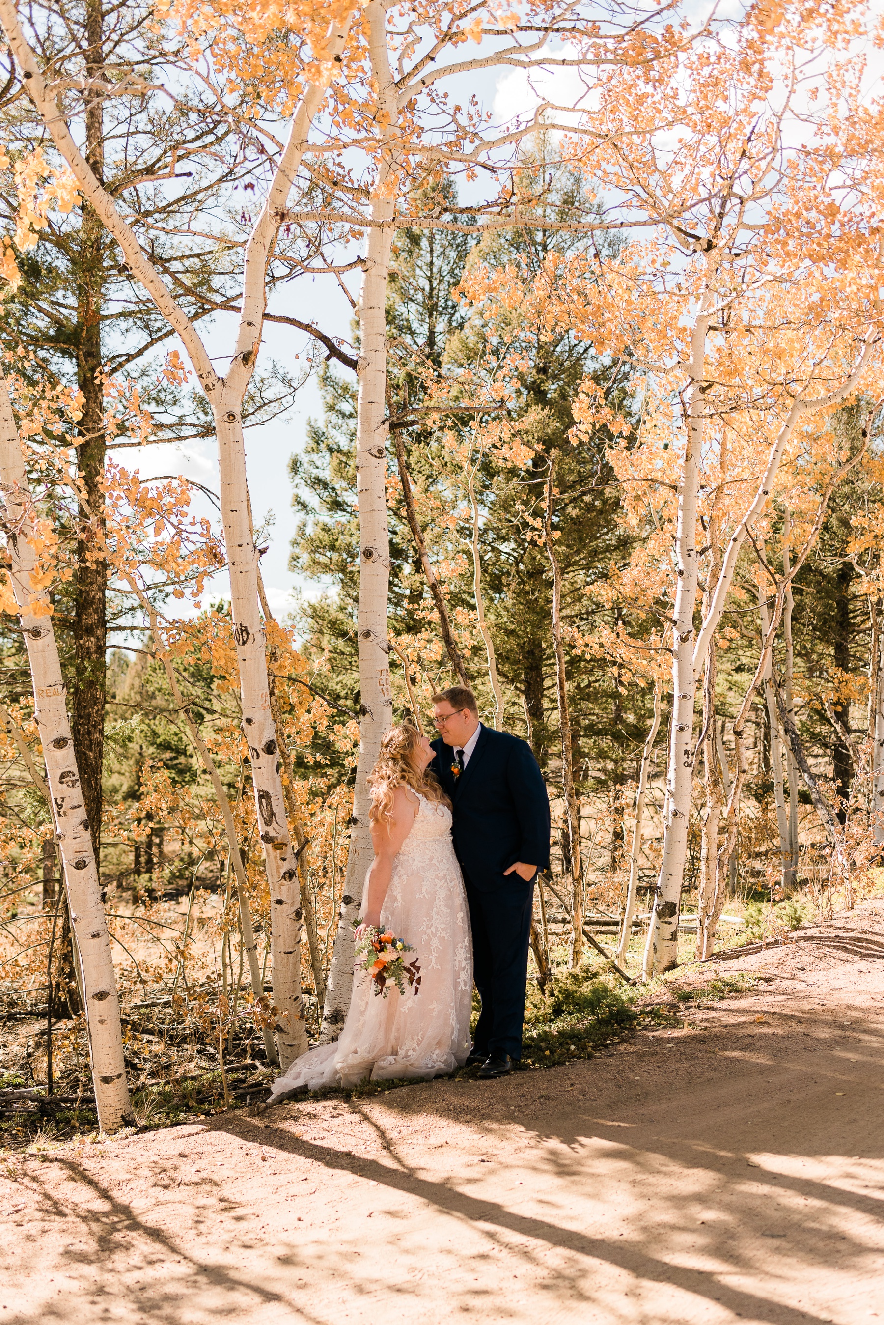 Bride and groom with aspen trees with yellow leaves behind them.