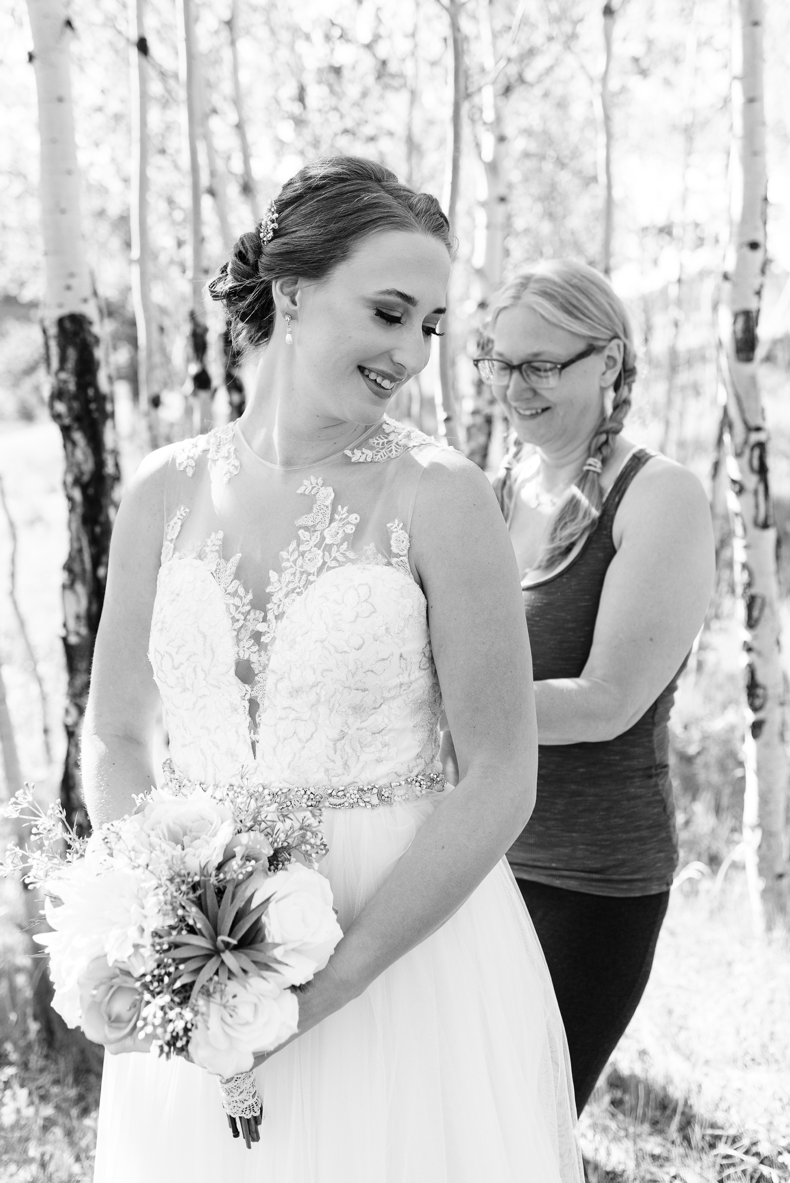 Bride's mom zipping up back of her dress and smiling