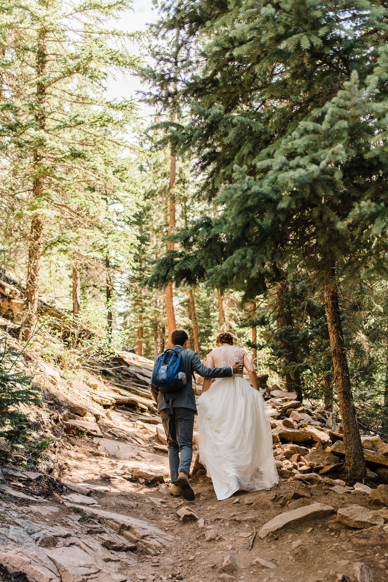 Groom with hand on bride's back leading up hiking trail