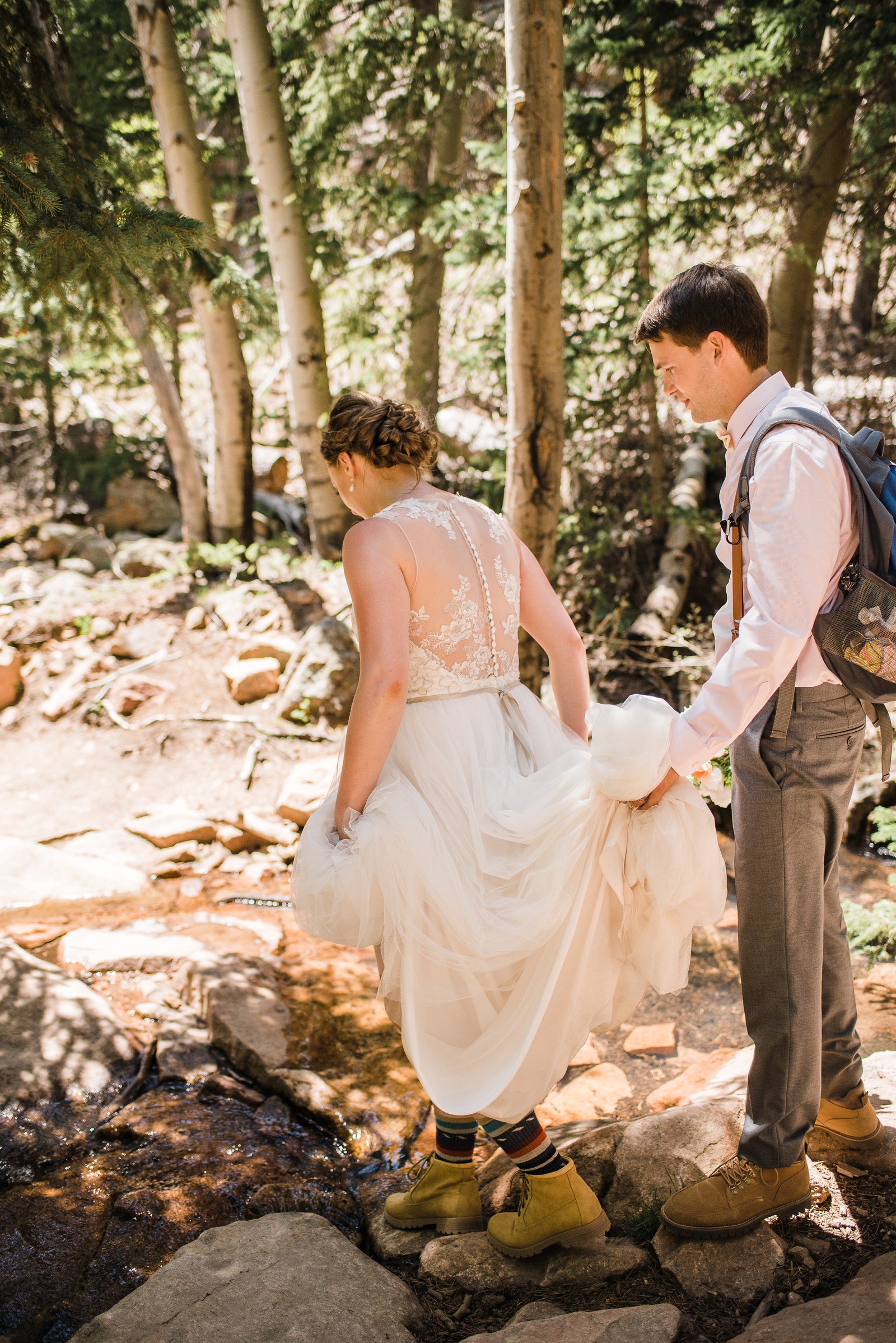 Groom holding bride's dress to cross stream.